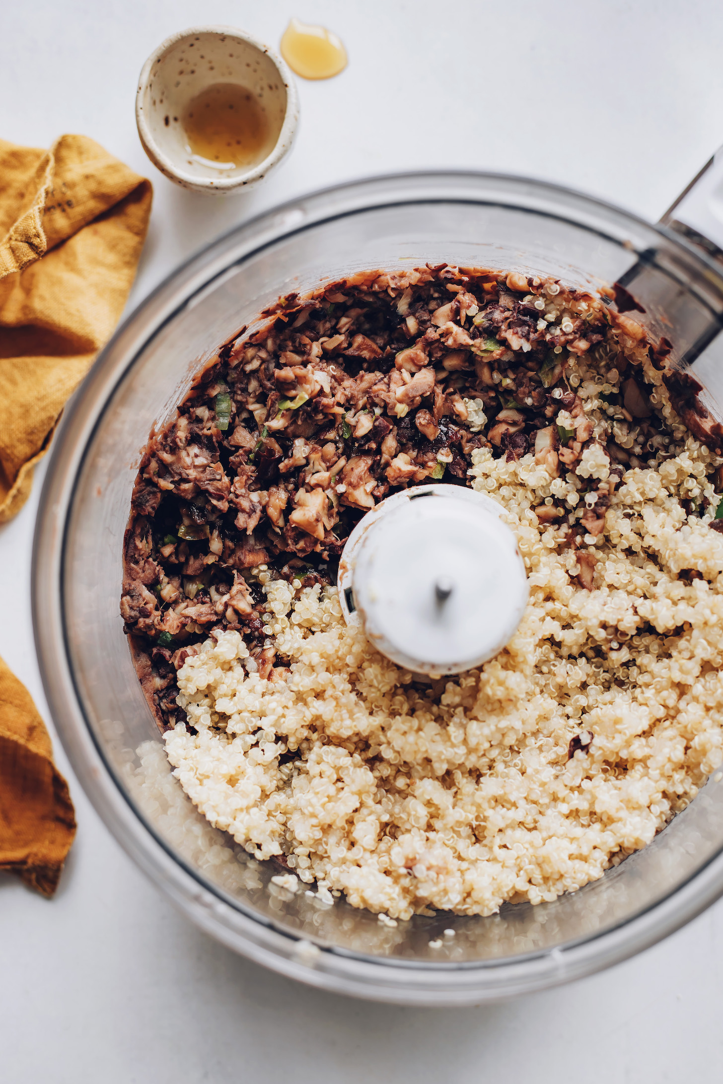Food processor with cooked quinoa over a black bean and mushroom mixture