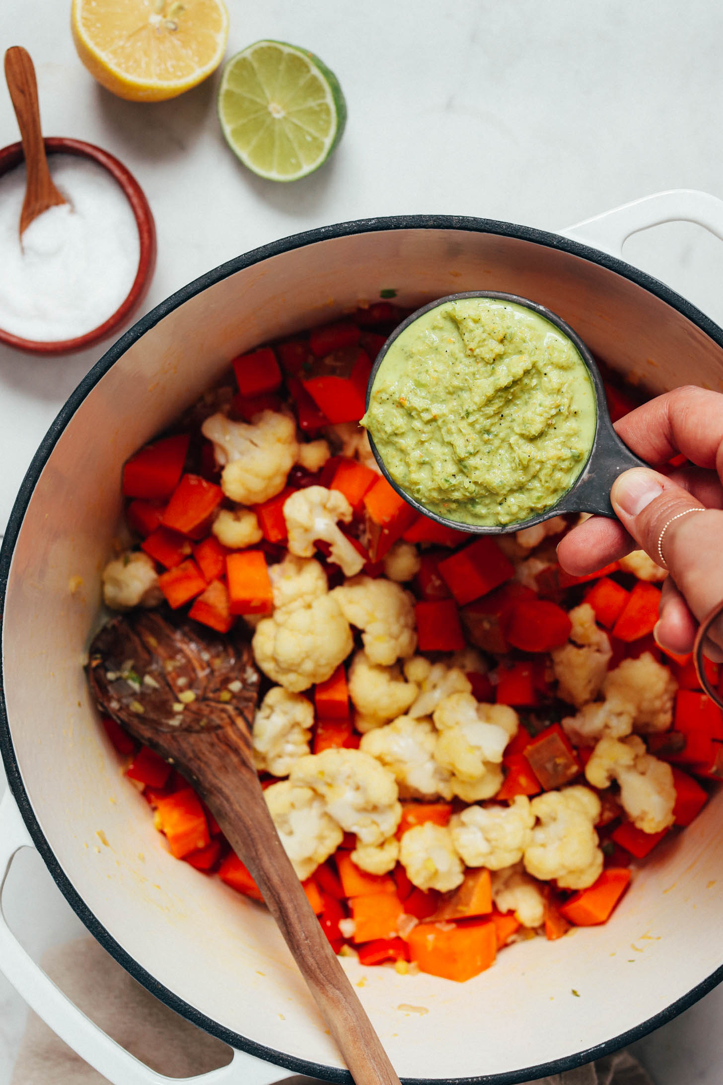 Holding a measuring cup of green curry paste over sautéed vegetables