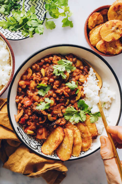 Holding a fork in a bowl of white rice, vegan picadillo, and plantains