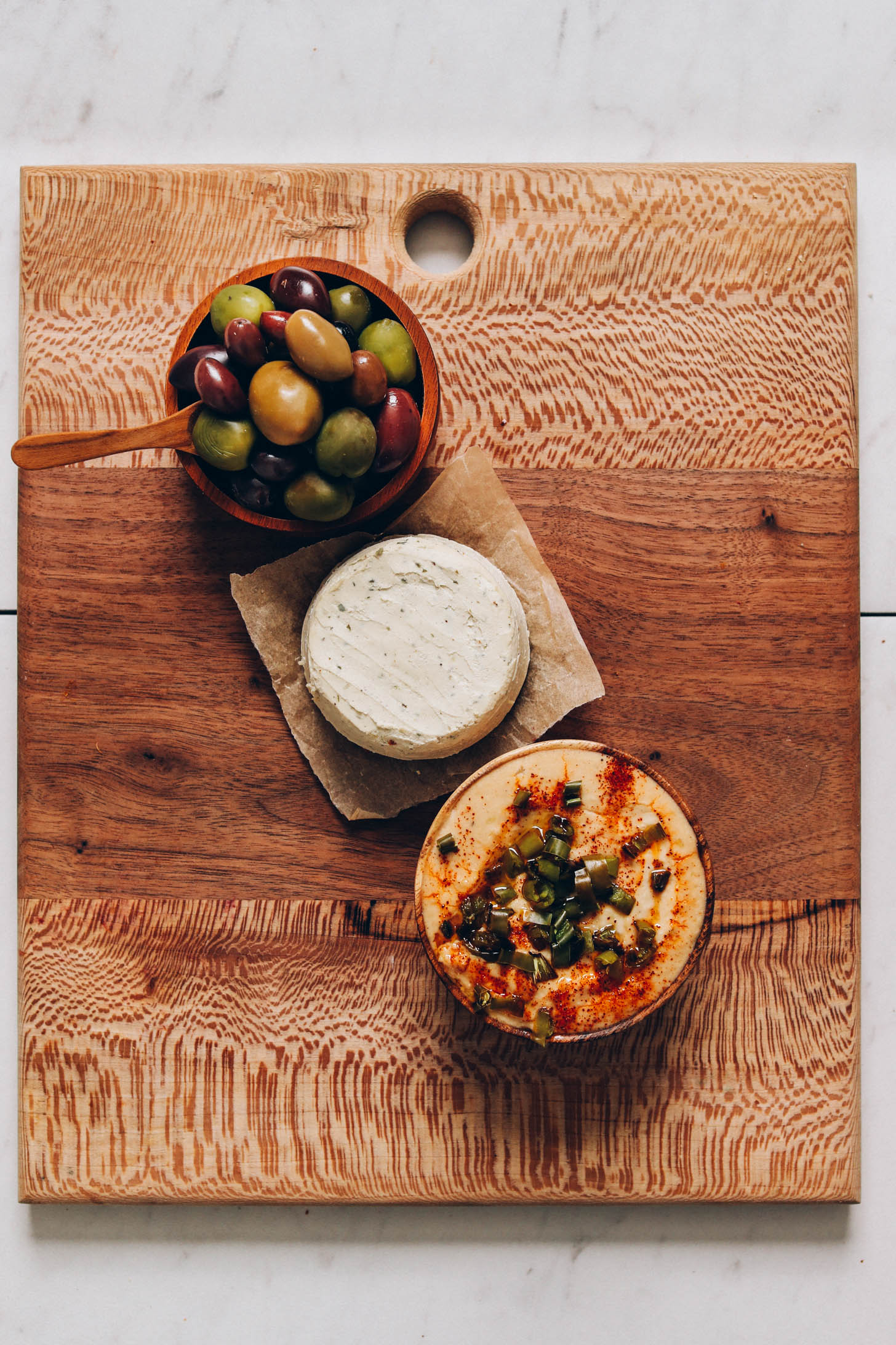 Wooden platter with olives, vegan cheese, and spicy dip