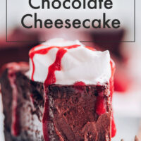 Slice of vegan and gluten-free easy baked chocolate cheesecake with vegan whipped cream and raspberry drizzle on top
