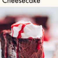 Slice of vegan and gluten-free easy baked chocolate cheesecake with vegan whipped cream and raspberry drizzle on top
