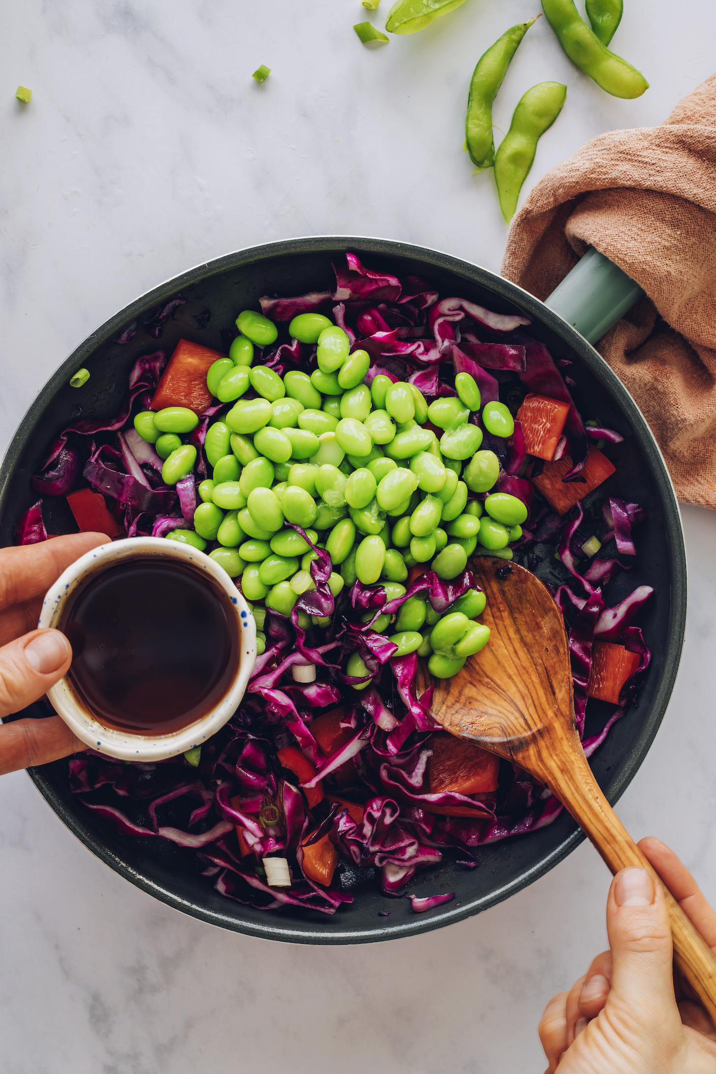 Holding a bowl of teriyaki sauce over sautéed veggies and shelled edamame