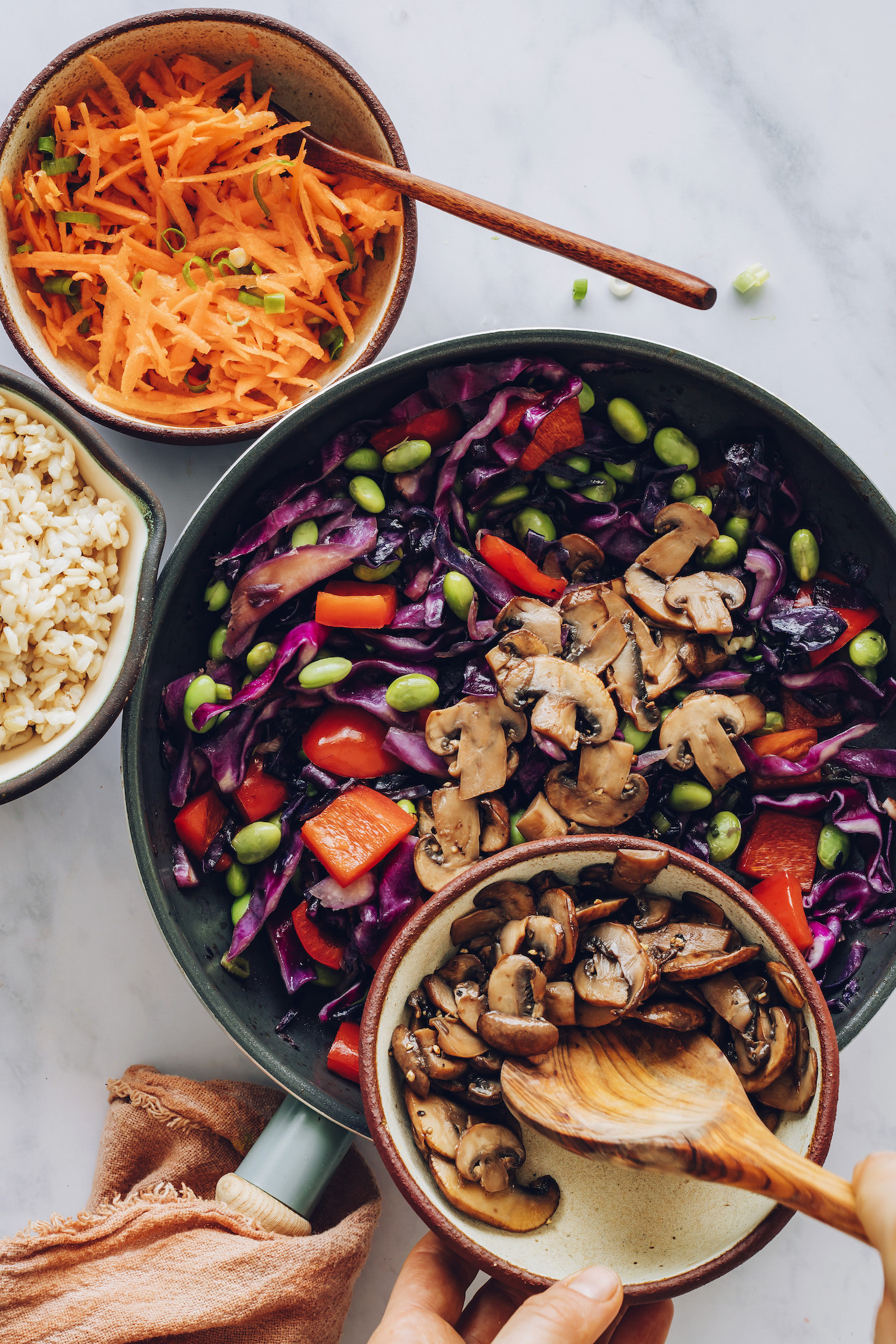 Adding mushrooms to a skillet of edamame and vegetables