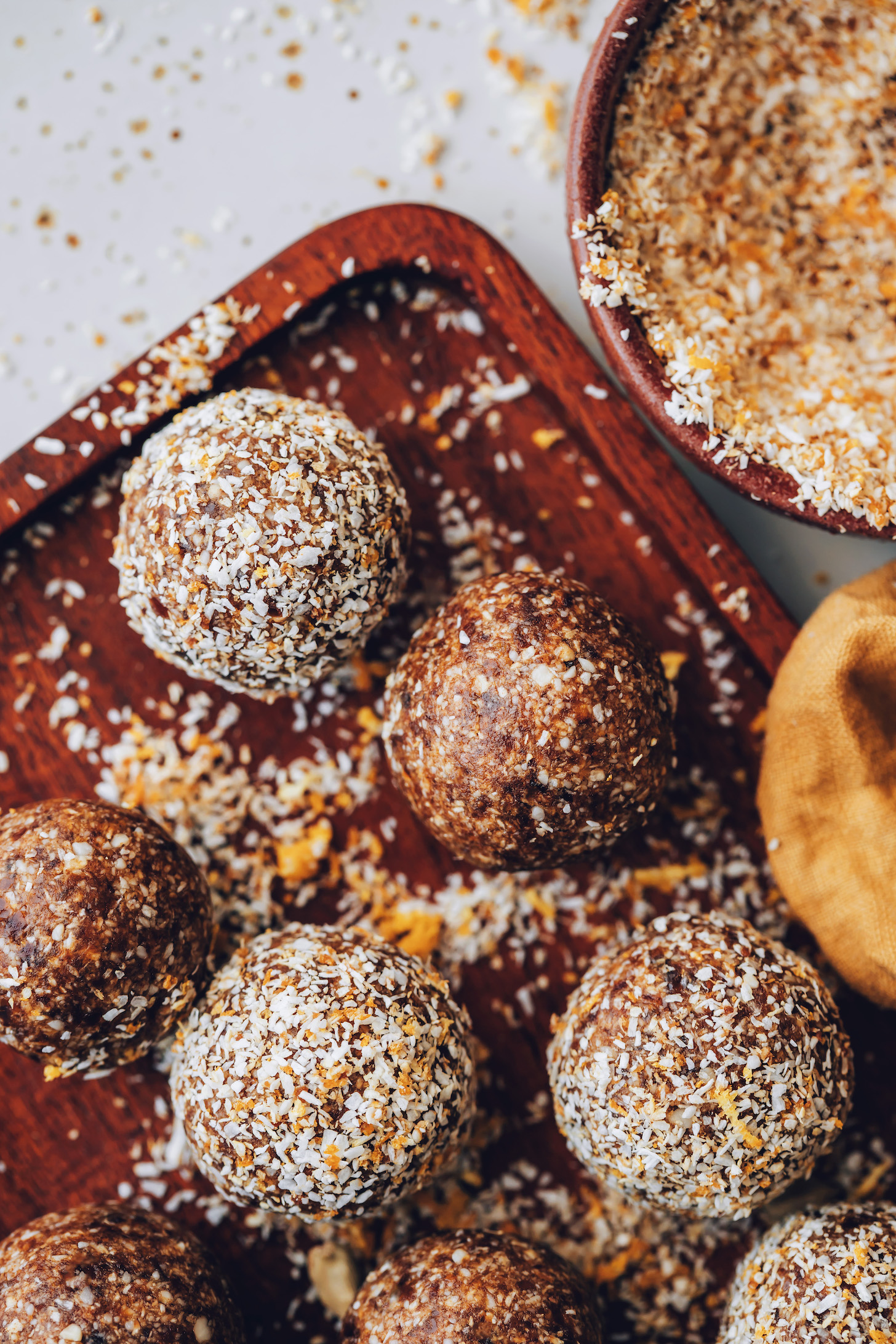 Wooden tray of orange cardamom energy bites with some coated in orange zest and coconut