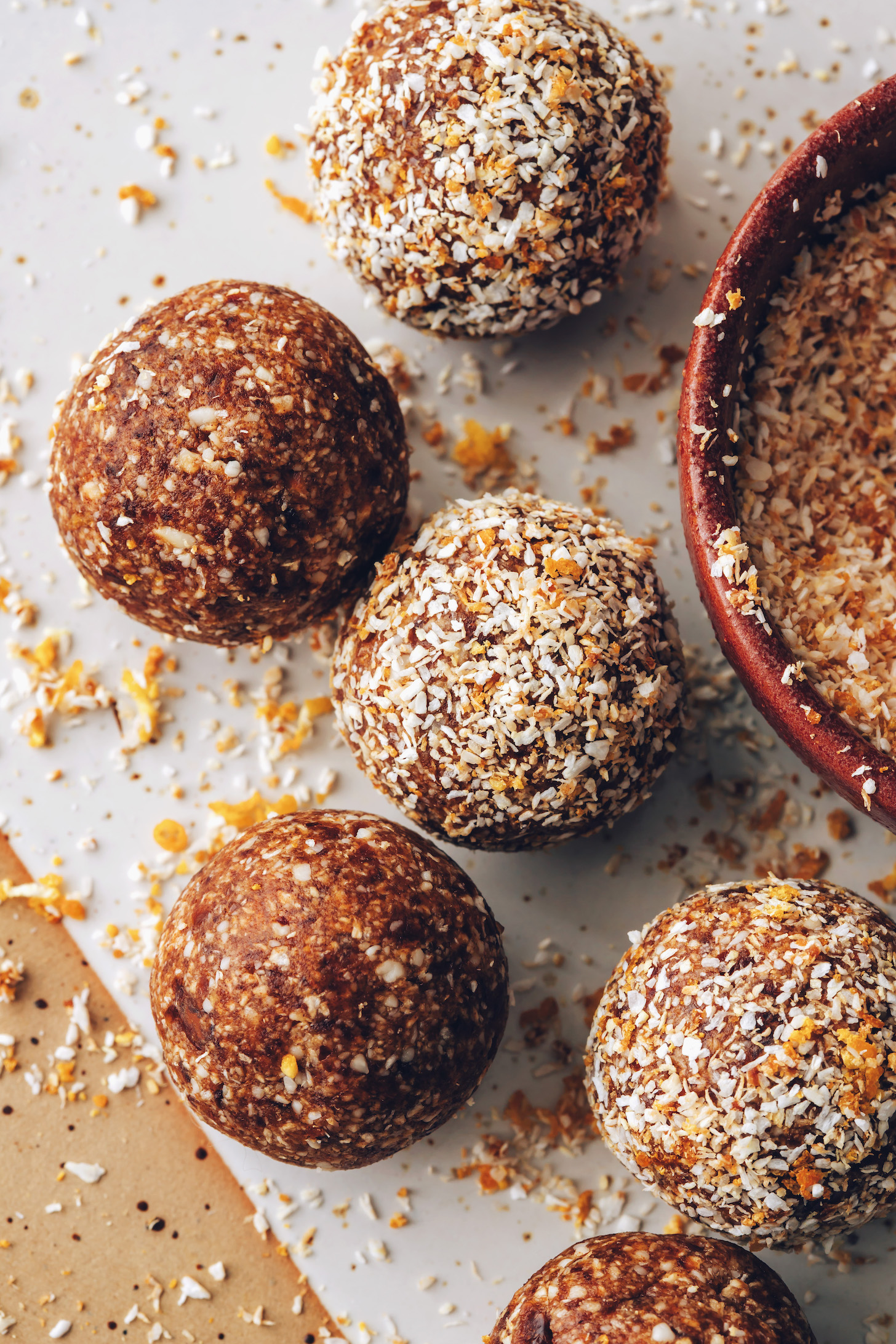 Orange cardamom energy bites on a ceramic platter next to a bowl of orange zest, coconut, and coconut sugar