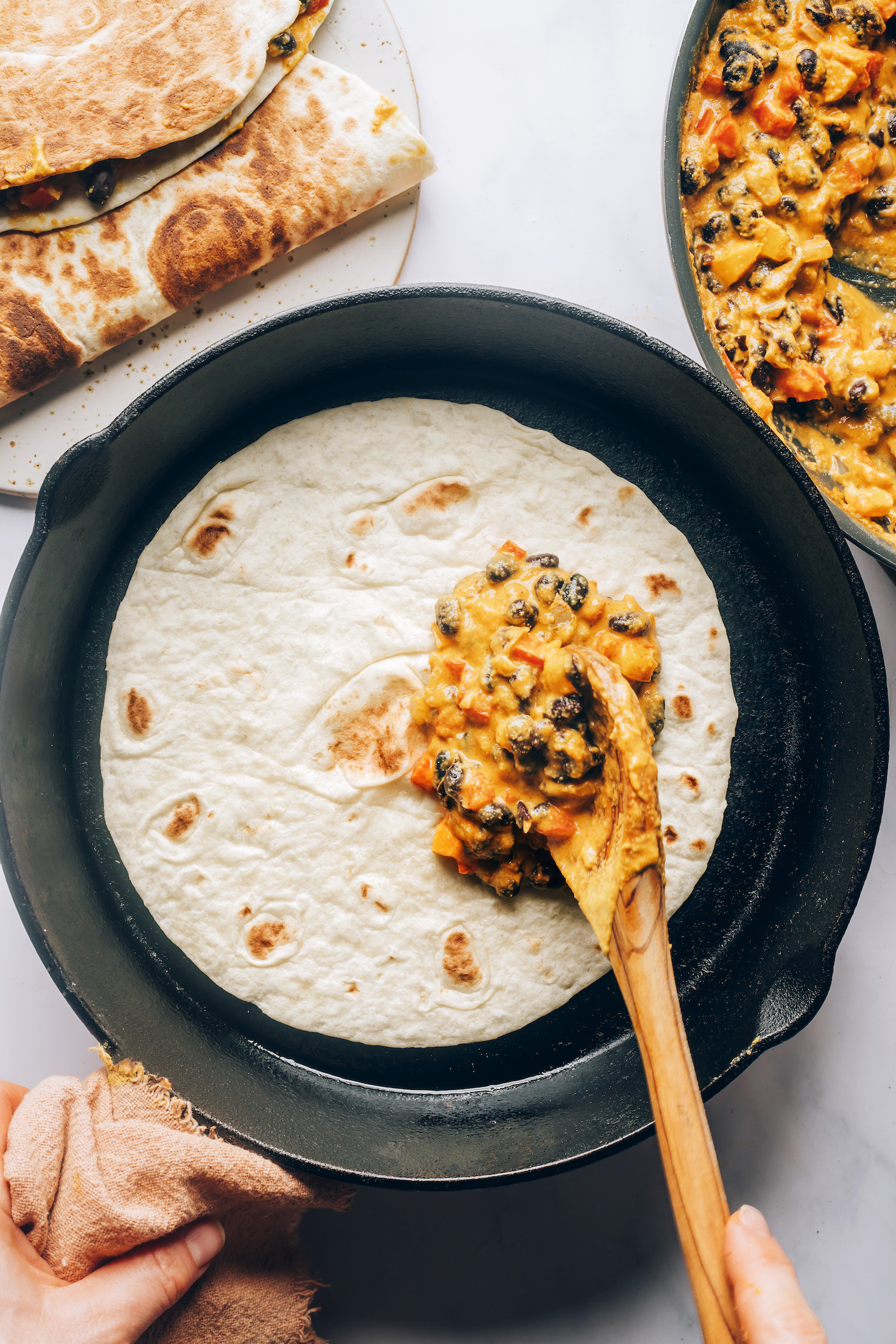 Adding vegan quesadilla filling onto a flour tortilla in a skillet