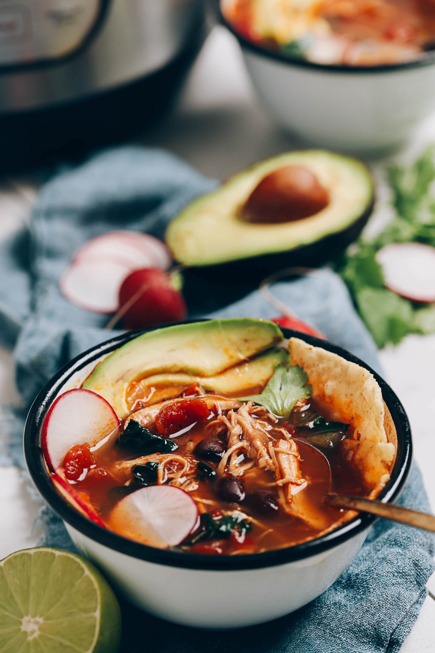 Bowl of chicken tortilla soup topped with cilantro, avocado, radish, and tortilla chips