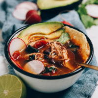 Bowl of chicken tortilla soup topped with avocado, sliced radish, and tortilla chips