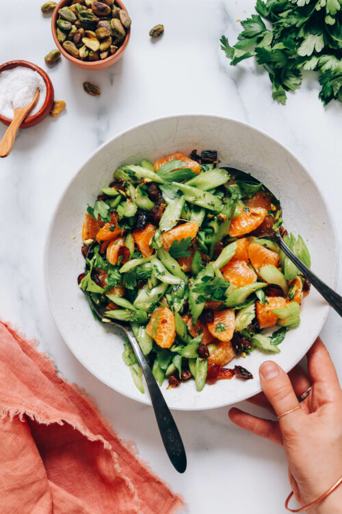 Holding a bowl of celery salad with dates, mandarins, and pistachios