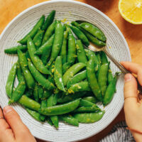 Holding a gold spoon in a bowl of sautéed sugar snap peas