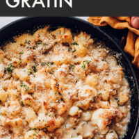 Skillet of vegan and gluten-free creamy cauliflower gratin with a wooden spoon in it