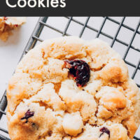 A vegan and gluten-free cranberry macadamia nut cookie on a cooling rack