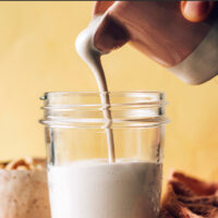 Hand pouring a container of vegan cashew cream into a jar