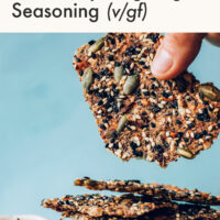 Hand holding an easy seed cracker with everything bagel seasoning over a stack of crackers