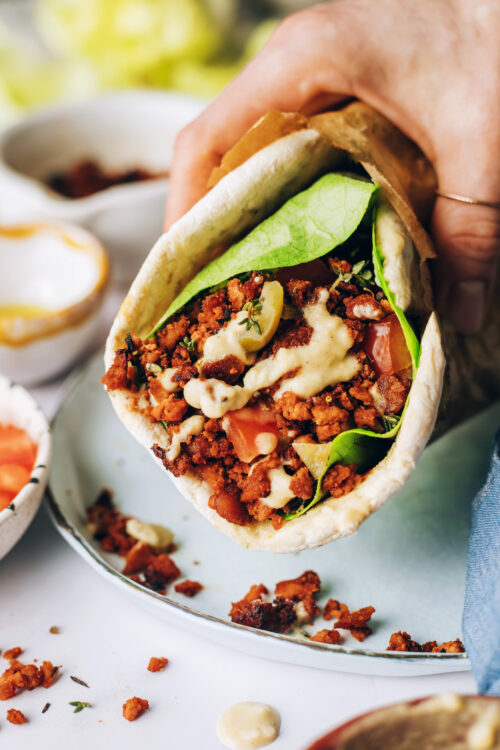 Holding a vegan wrap made with crispy tofu, veggies, and hummus dressing