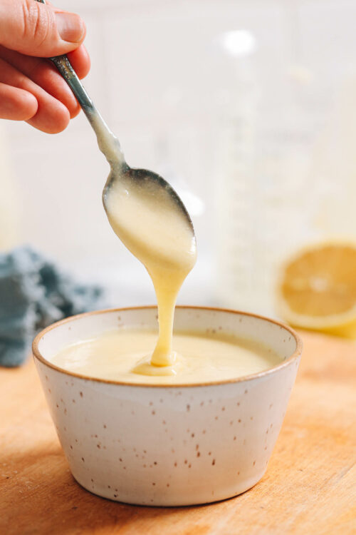 Vegan hollandaise sauce dripping from a spoon into a bowl