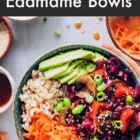 Hands holding a vegan and gluten-free rainbow vegetable edamame bowl with teriyaki sauce