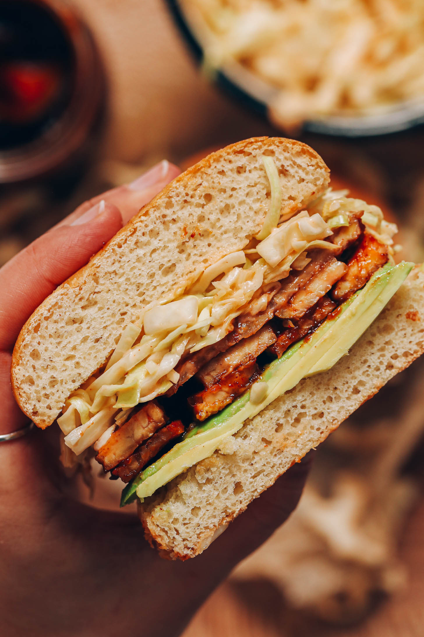 Close up shot of a hand holding a BBQ tempeh sandwich