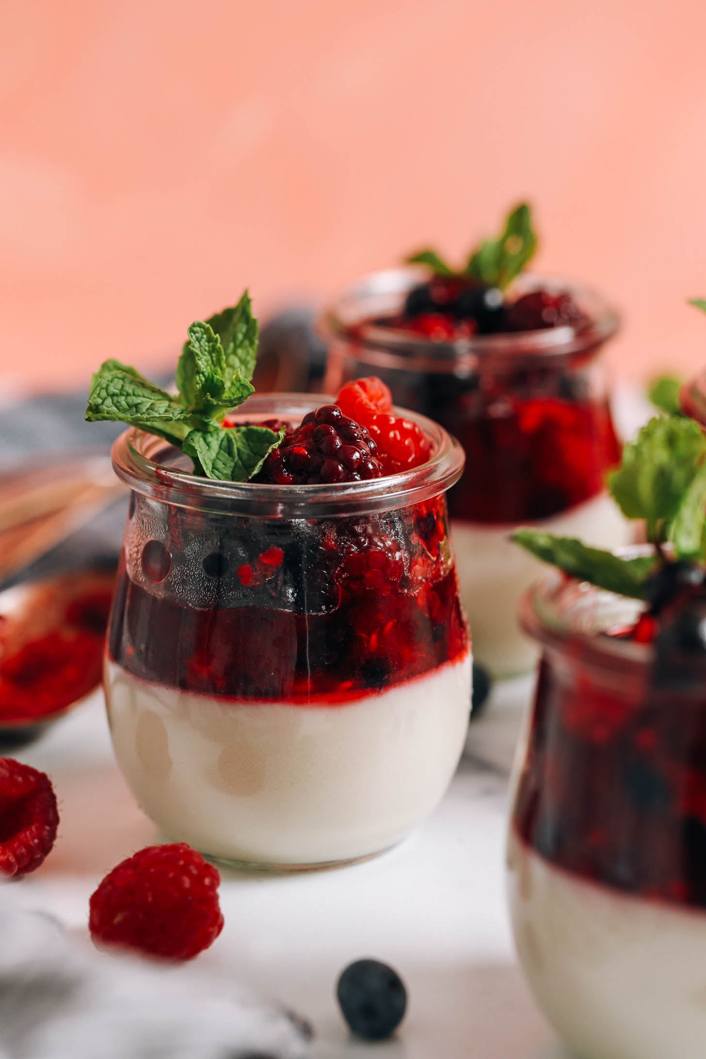 Jars of dairy free panna cotta topped with bubbly mixed berries and fresh mint leaves
