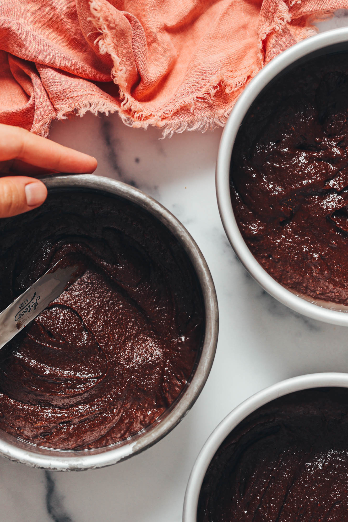 Spreading chocolate cake batter into a round cake pan