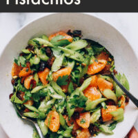 Hand holding a bowl of vegan and gluten-free vibrant celery salad with dates and pistachios