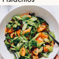 Hand holding a bowl of vegan and gluten-free vibrant celery salad with dates and pistachios