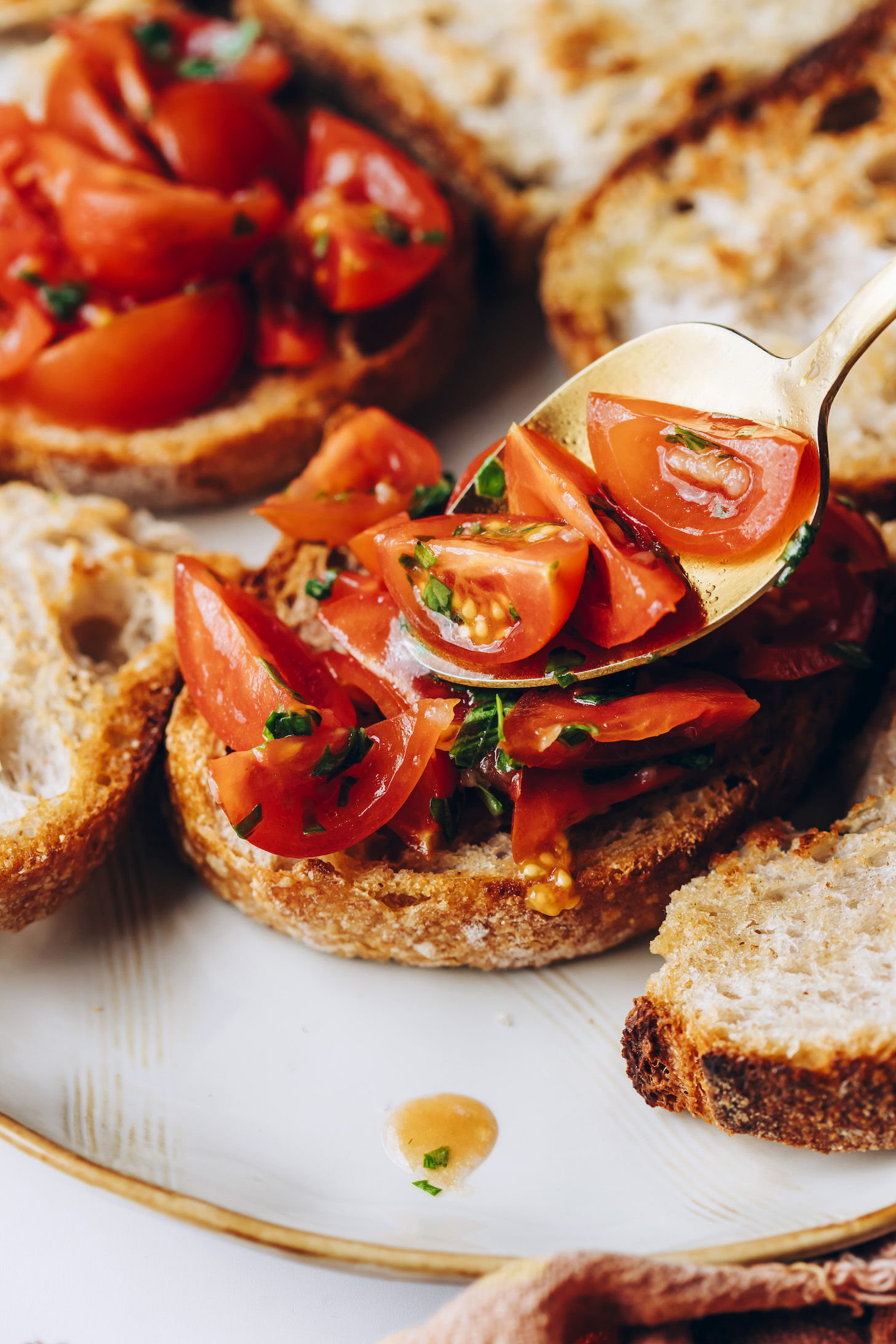 Using a spoon to transfer a cherry tomato and basil mixture onto toasted bread