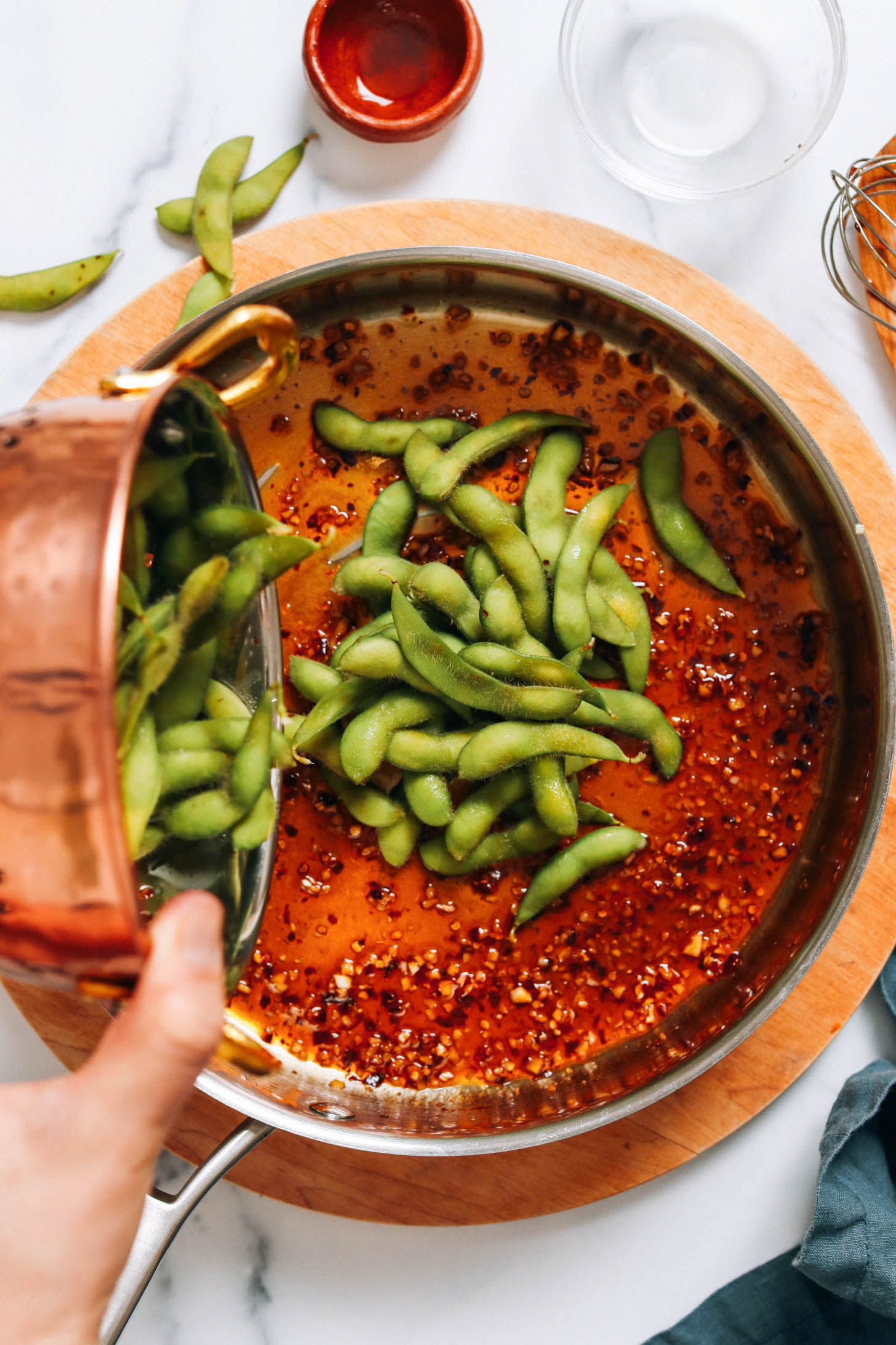 Adding edamame pods to a skillet of sauce