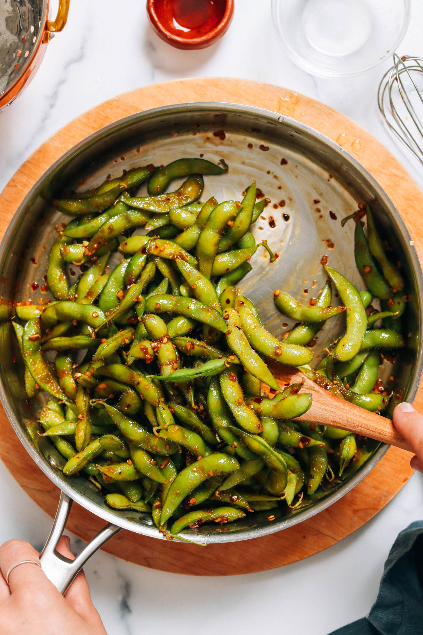 Stirring edamame pods in a sticky sauce