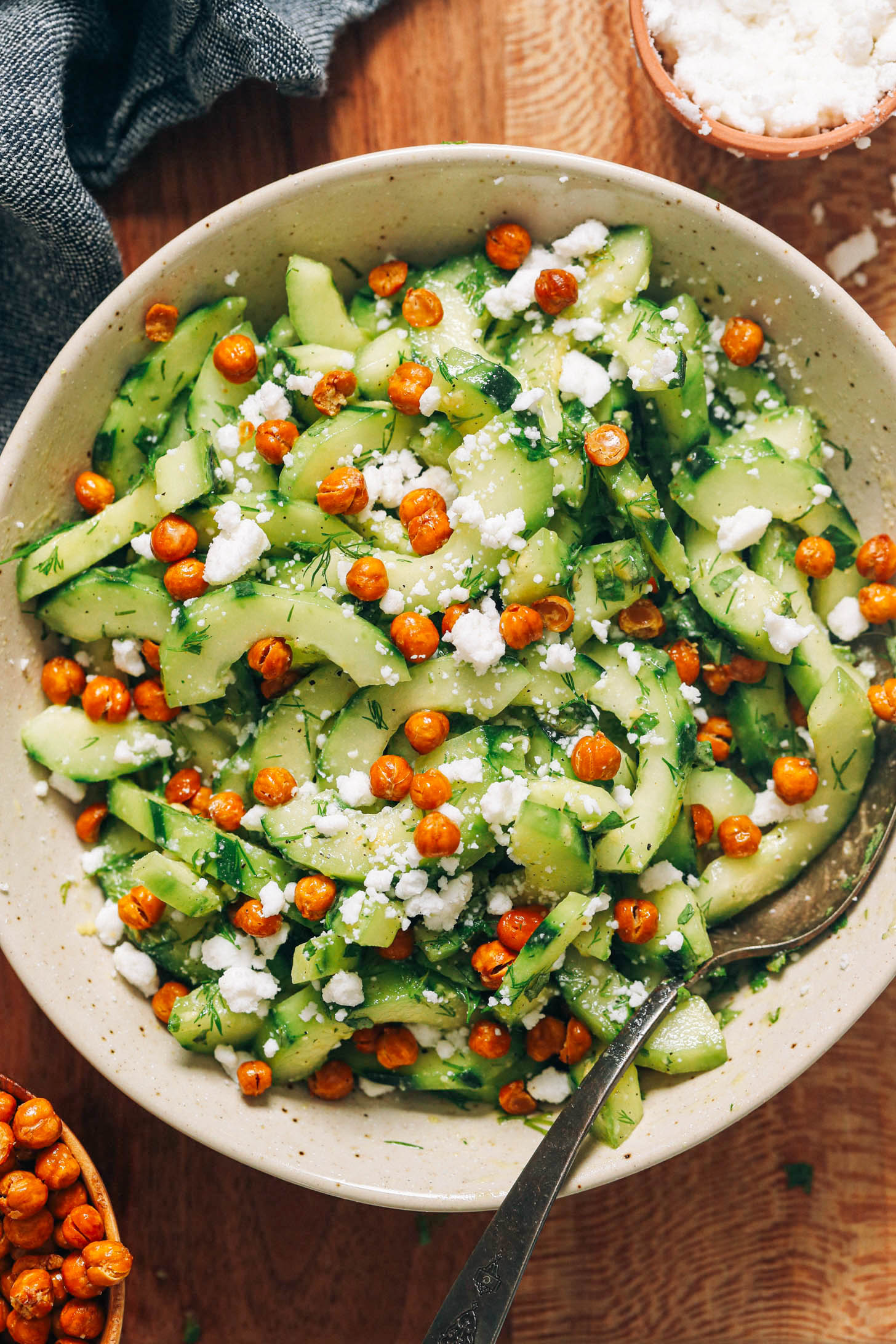 Large serving bowl filled with herbed cucumber salad and topped with vegan feta and crispy chickpeas