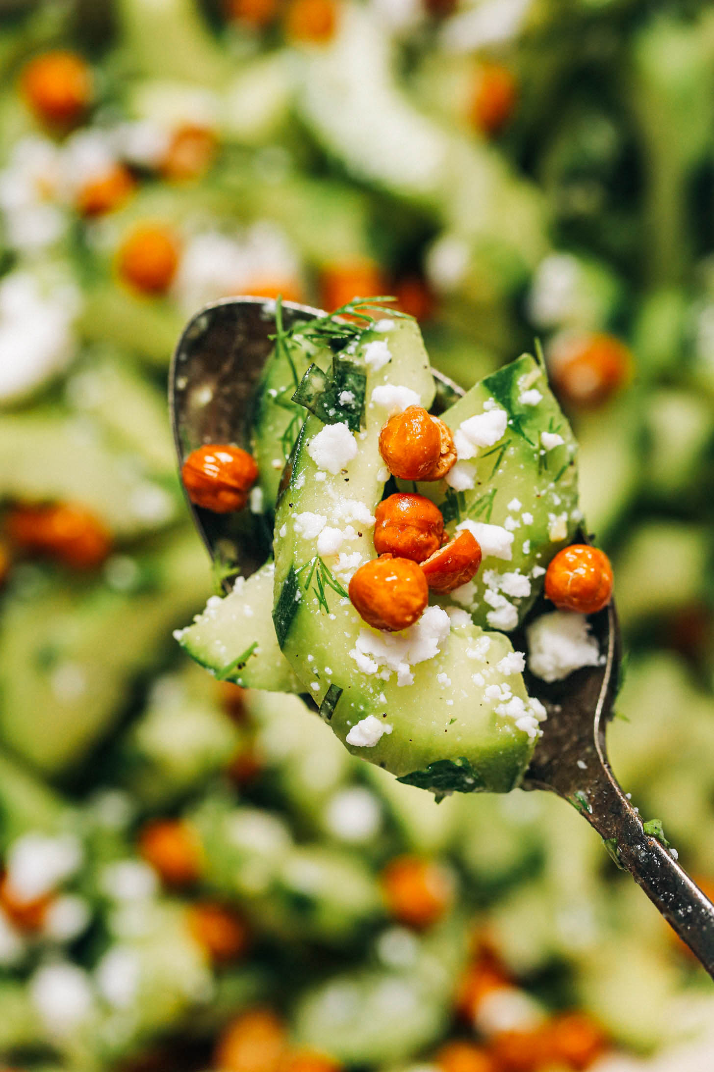 Close up shot of sliced cucumbers with crispy chickpeas, vegan feta, and fresh herbs
