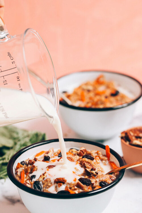 Pouring dairy-free milk into a bowl of carrot cake oatmeal