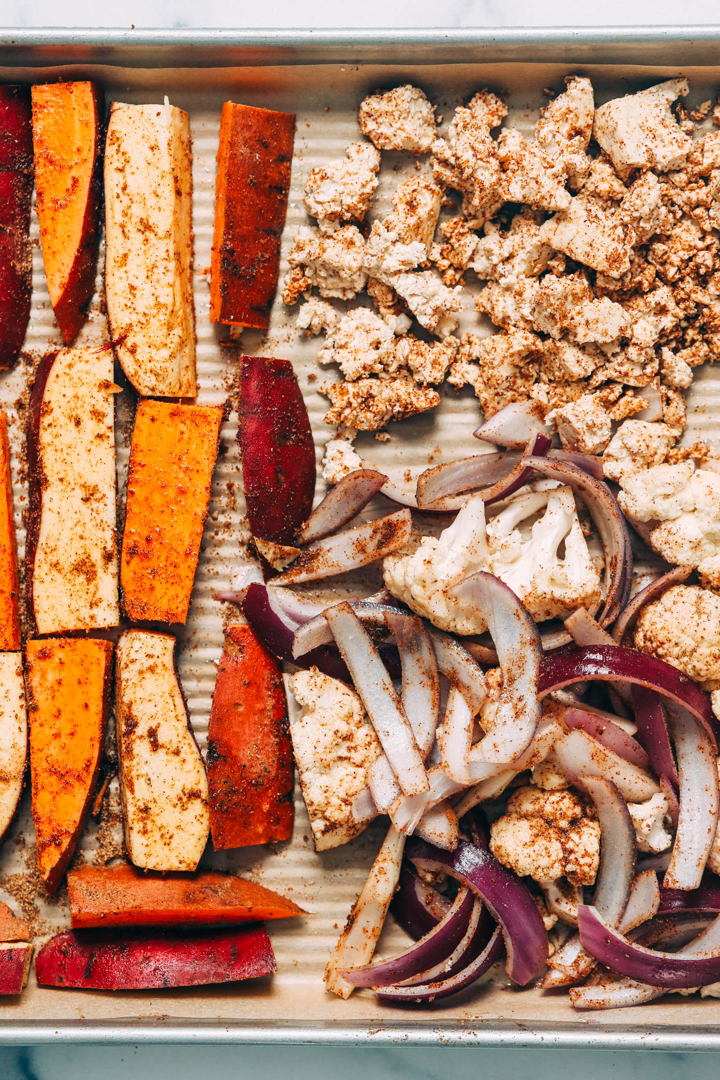 Baking sheet of chopped sweet potato, red onion, and cauliflower seasoned with tandoori masala