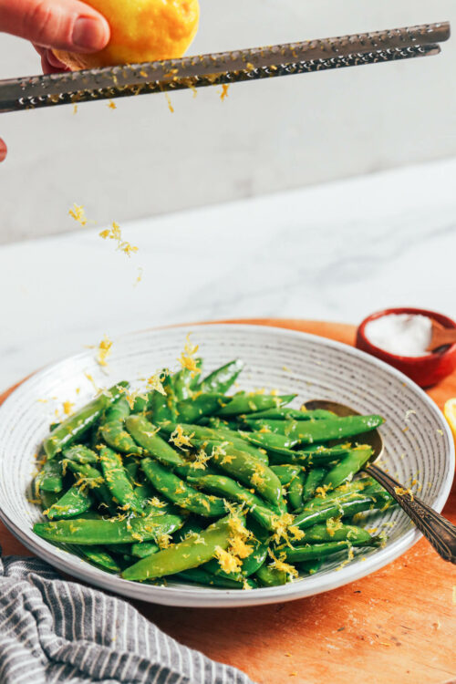 Zesting a lemon over a bowl of perfectly cooked sugar snap peas