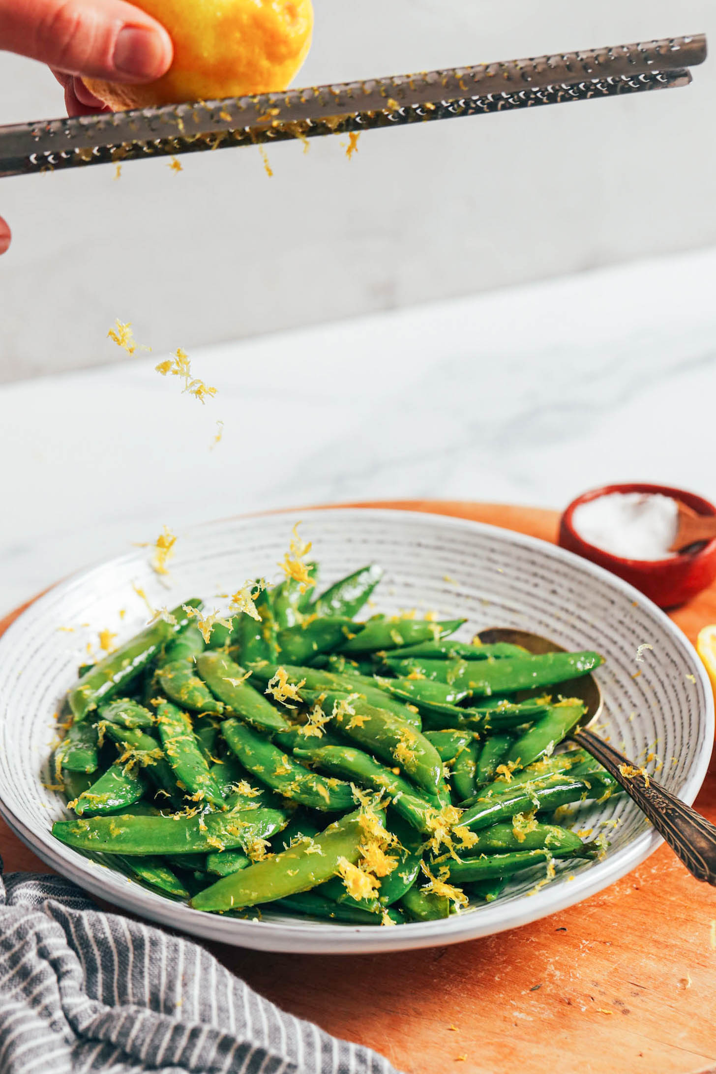 Zesting a lemon over a bowl of perfectly cooked sugar snap peas