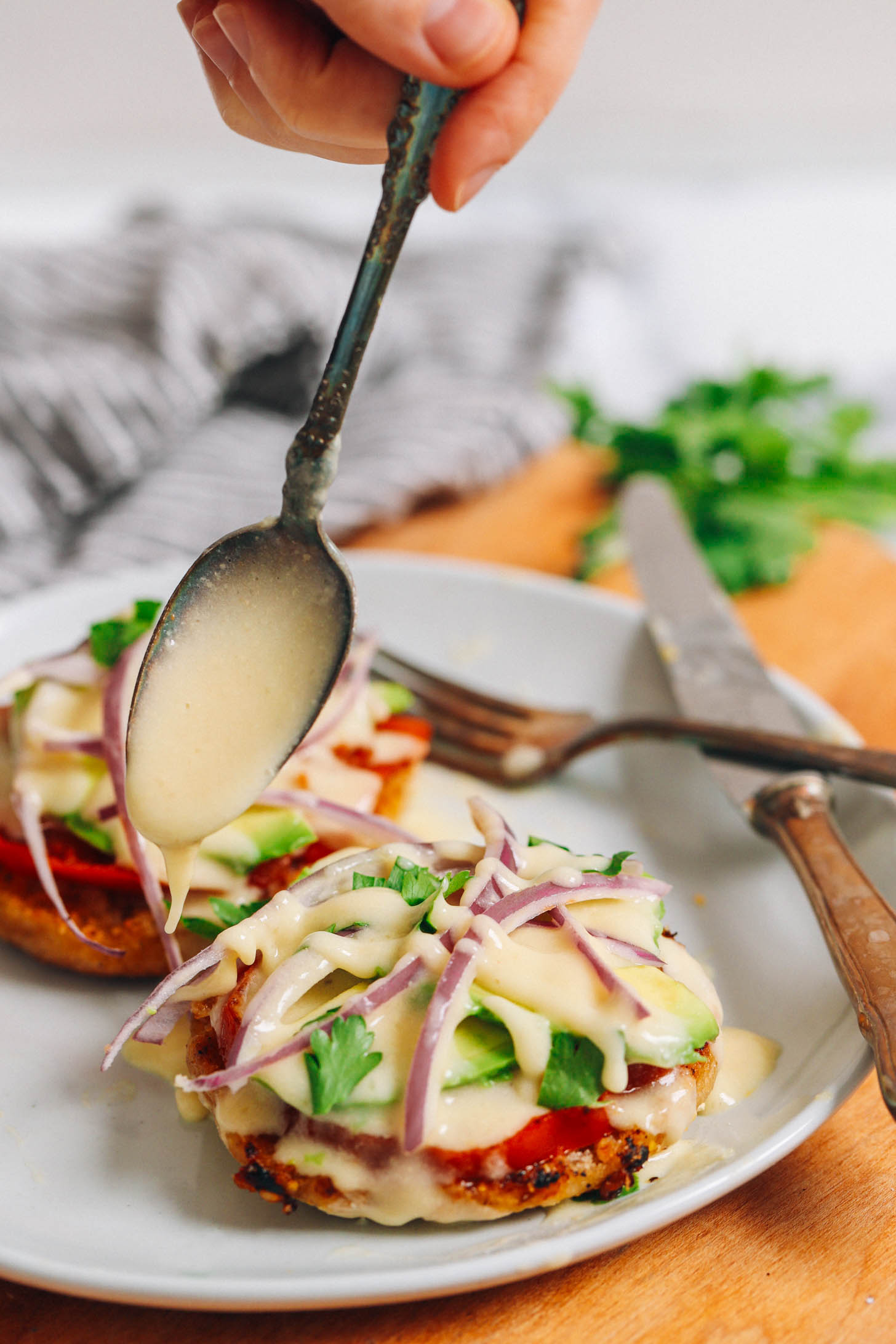 Drizzling vegan hollandaise sauce over an eggless benedict