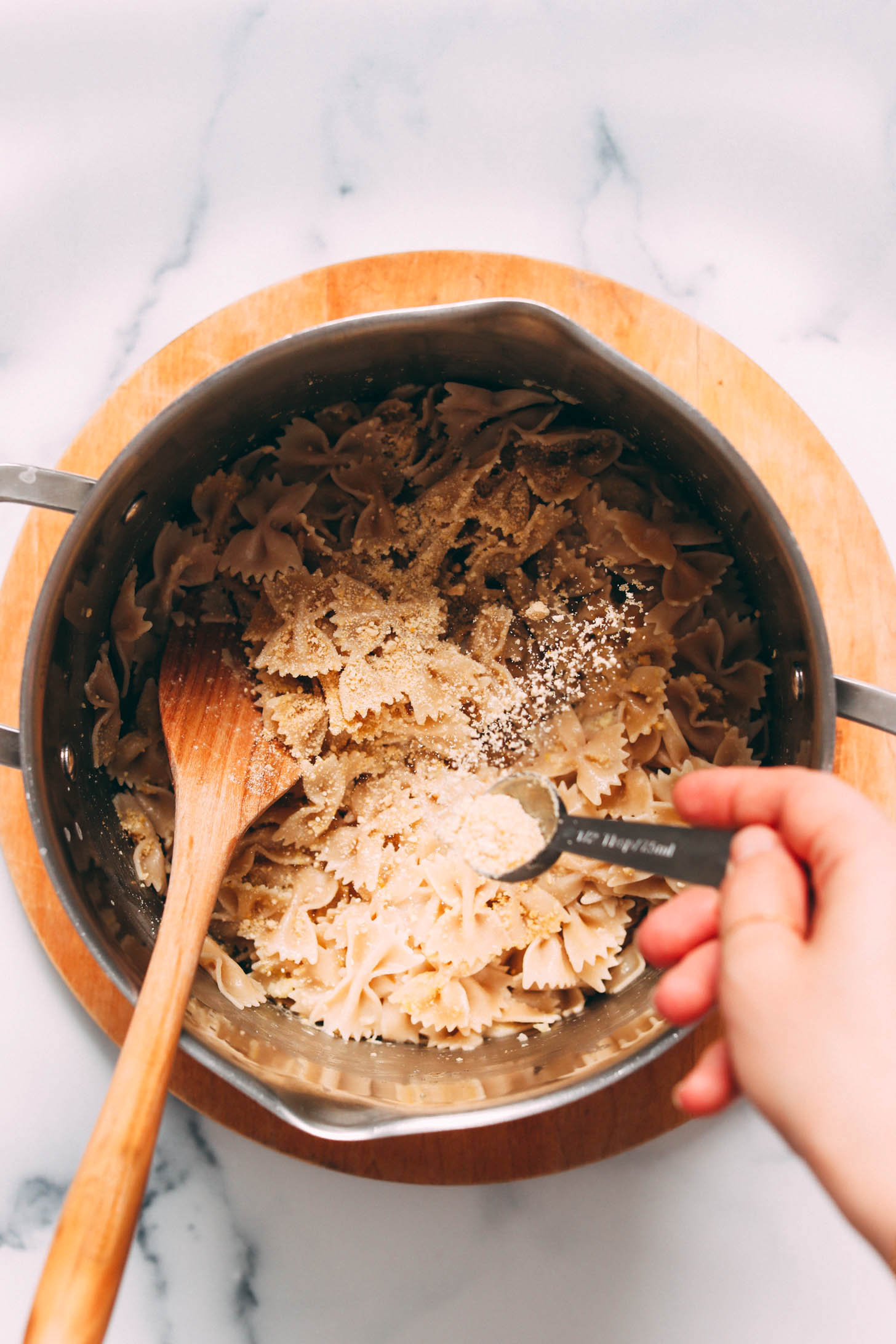 Sprinkling vegan parmesan cheese into a pot of pasta