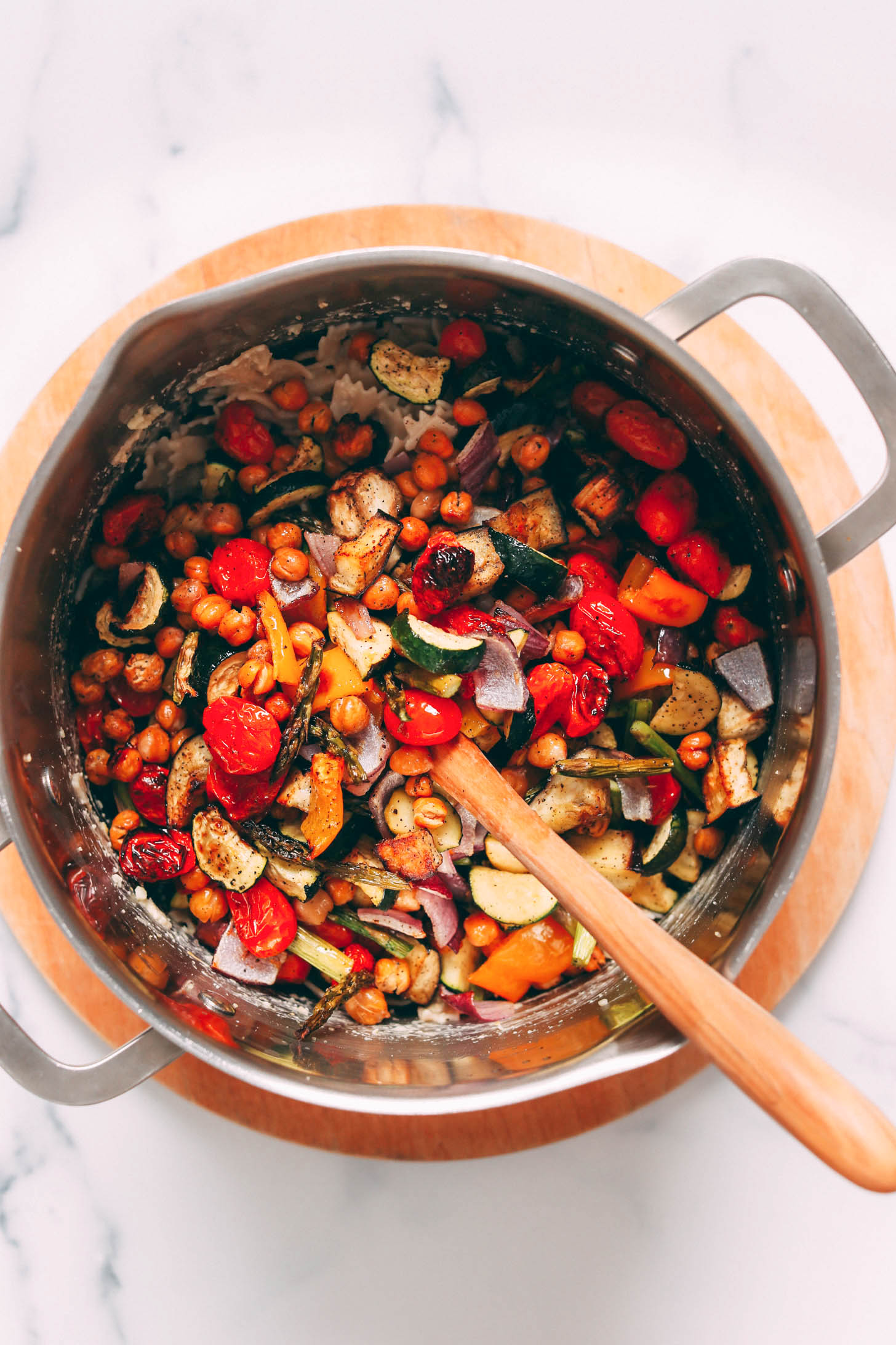 Wooden spoon in a pot of pasta topped with roasted vegetables