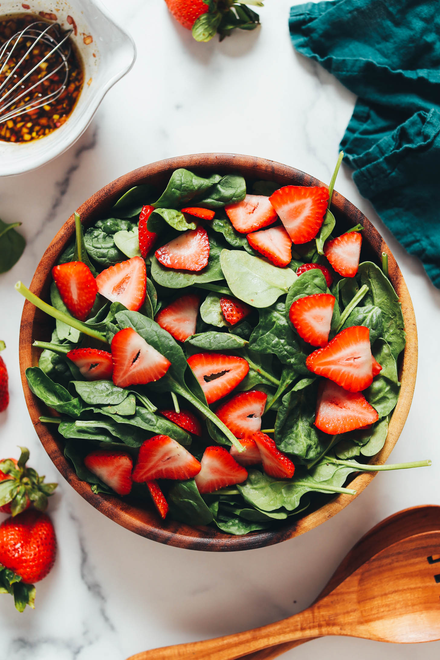 Balsamic dressing next to a bowl of baby spinach and sliced strawberries