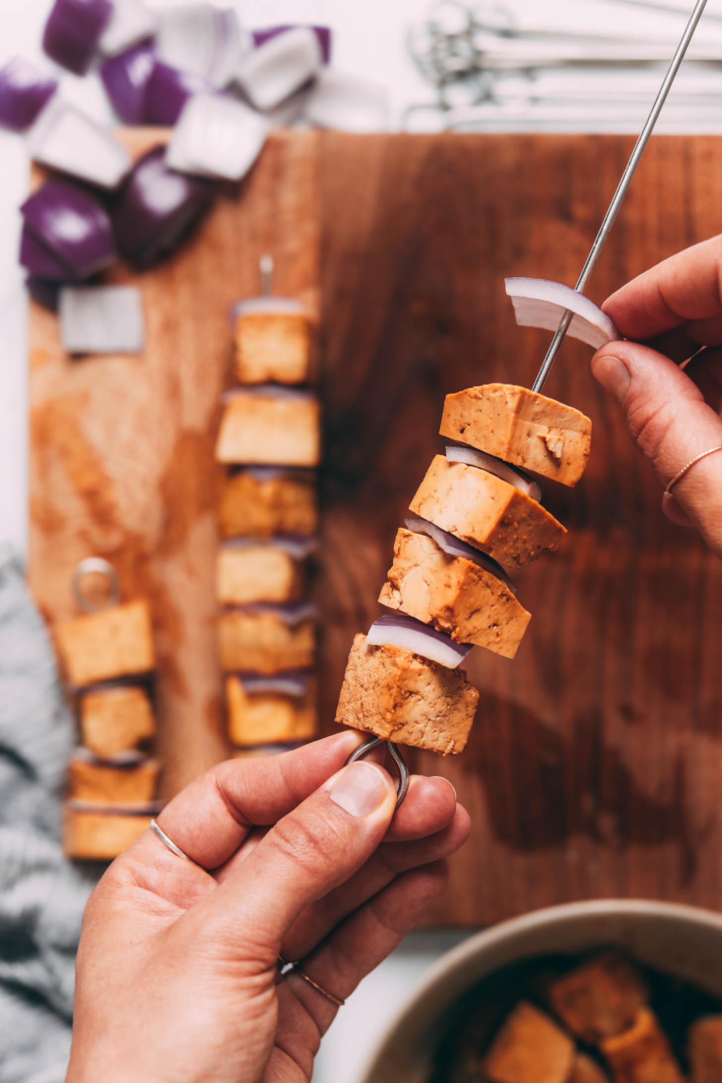 Adding a slice of red onion onto a skewer with cubed tofu and red onions