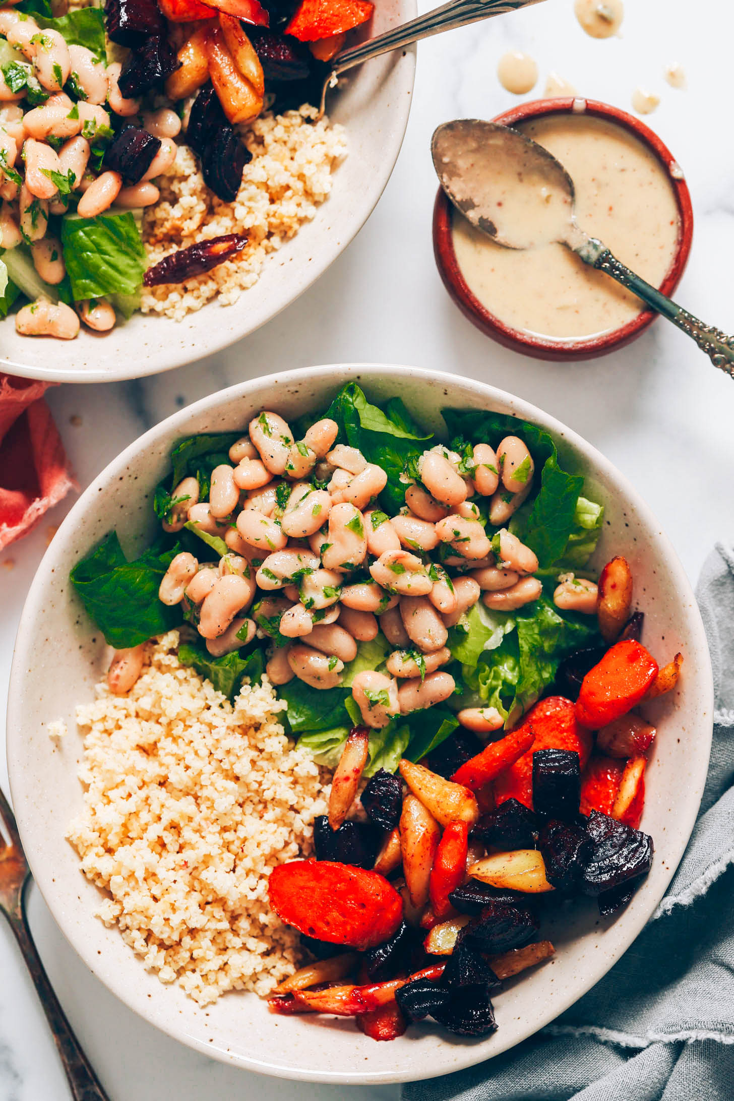 White bean caesar salad bowls next to a spoon over a bowl of vegan caesar dressing