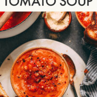 Overhead shot of a bowl of garlicky tomato white bean soup on a plate with a grilled cheese sandwich