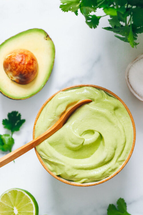 Bowl of avocado crema next to cilantro, avocado, lime juice, and salt