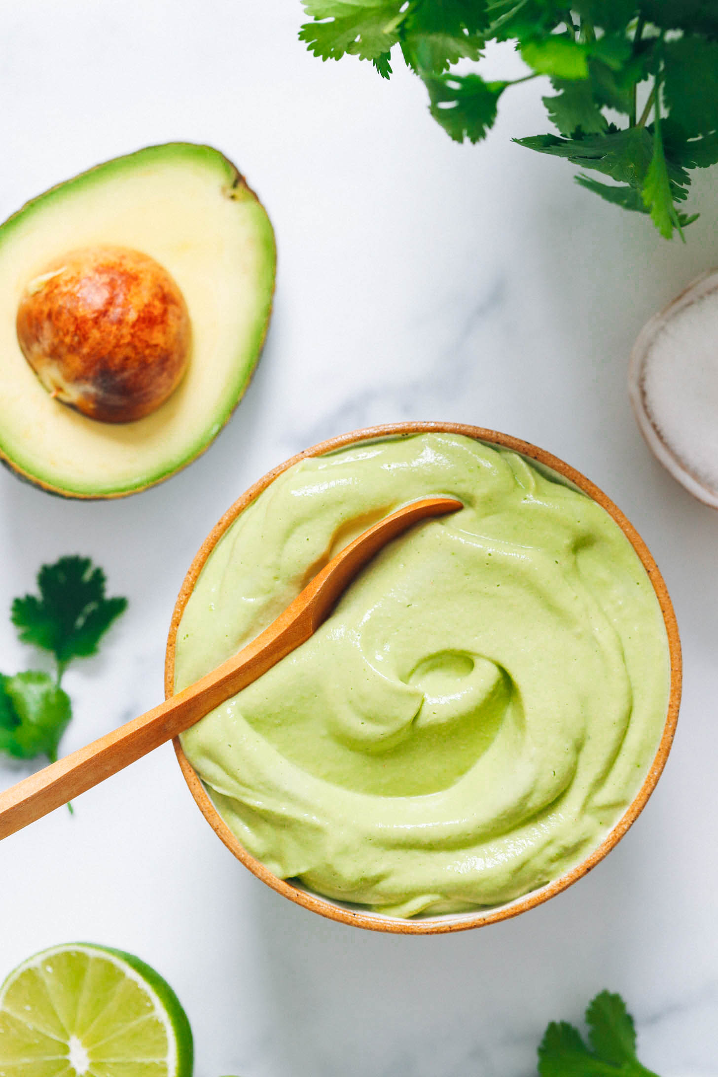 Bowl of avocado crema next to cilantro, avocado, lime juice, and salt