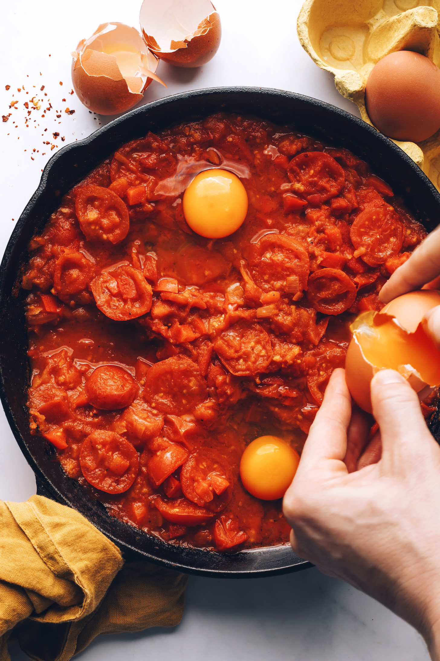 Cracking eggs into a skillet of shakshuka