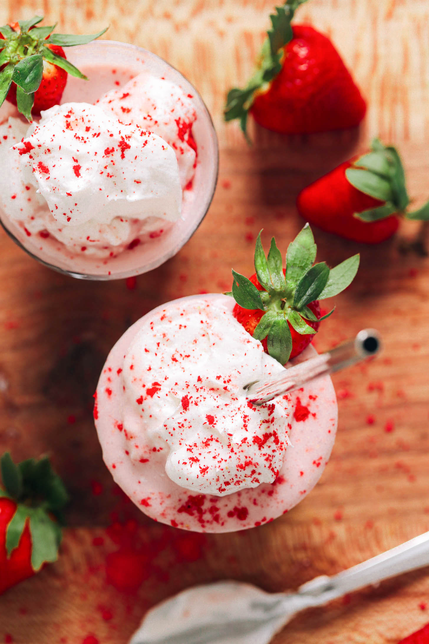 Overhead shot of two vegan strawberry milkshakes topped with coconut whipped cream and freeze dried strawberries