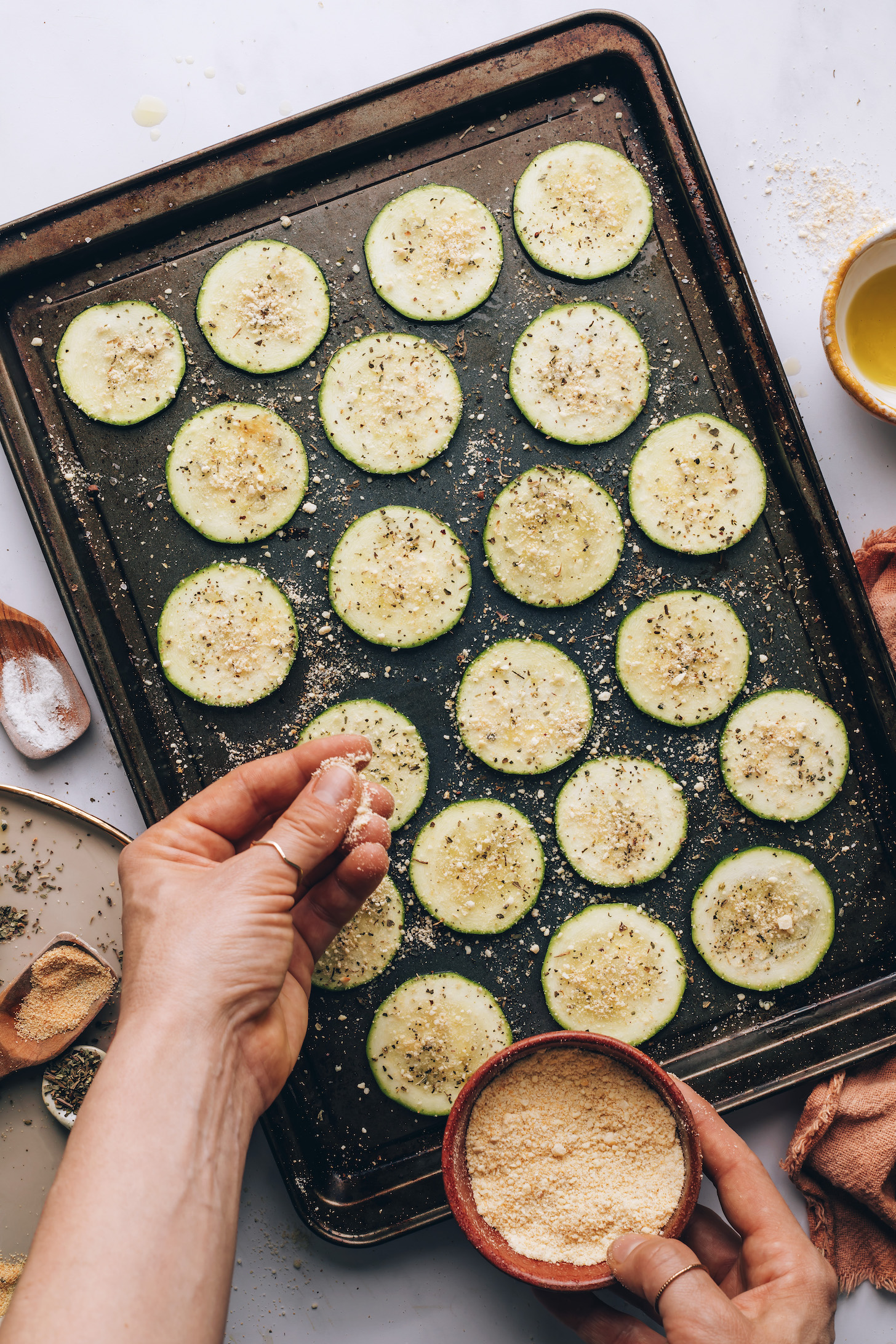 Sprinkling vegan parmesan cheese onto sliced zucchini