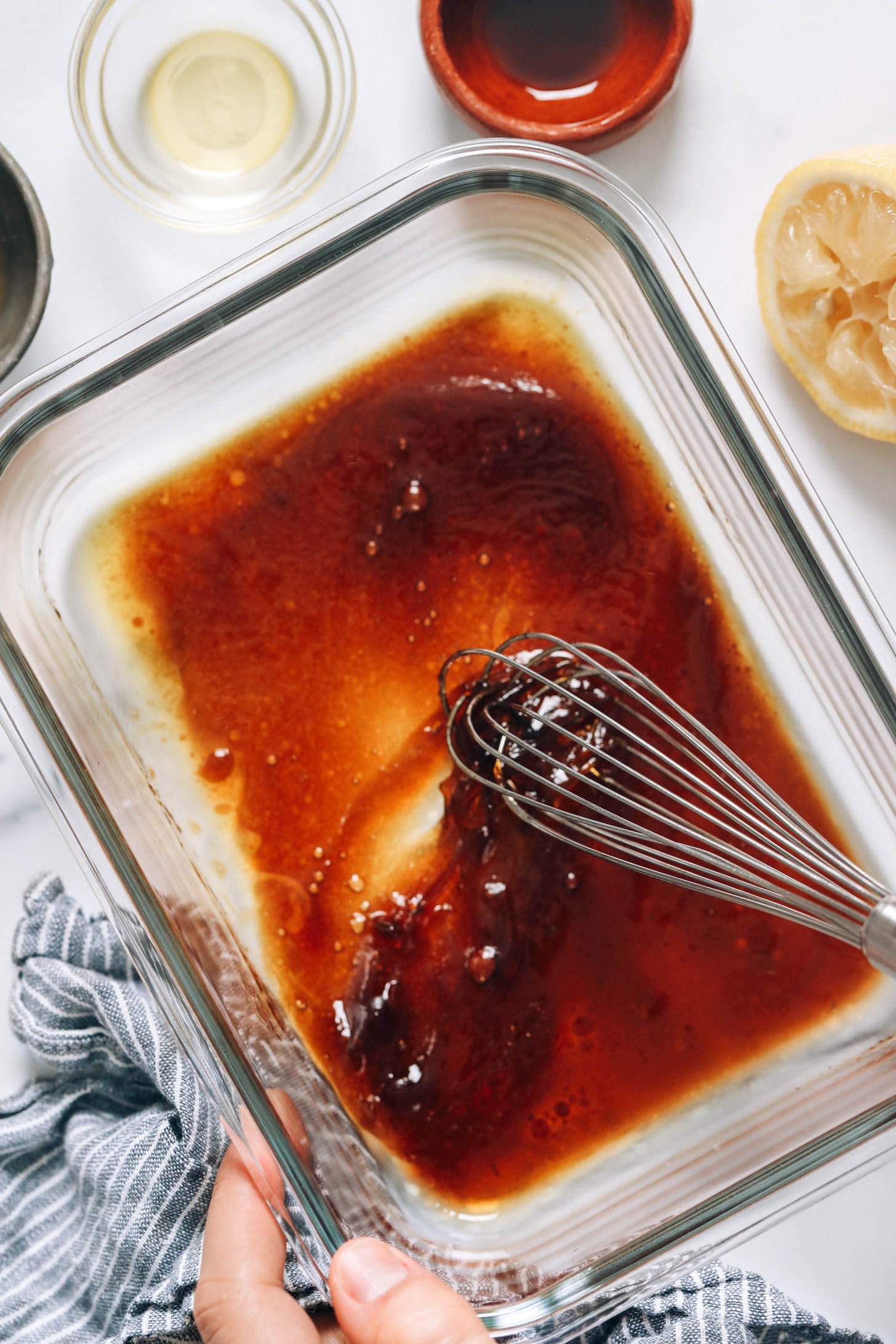 Whisking olive oil, coconut aminos, lemon juice, and maple syrup in a glass dish