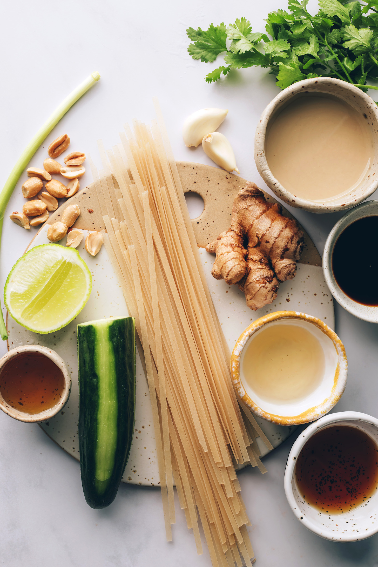 Cilantro, tahini, soy sauce, ginger, rice vinegar, maple syrup, noodles, cucumber, sesame oil, lime, peanuts, green onion, and garlic